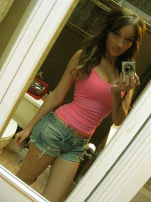 amateur pic This brunette girl, taking a selfie in the bathroom, is hot and has nice cleavage. She has blue nails, a tattoo, and is wearing a pink shirt and jean 