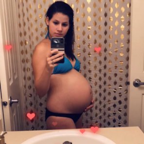 zdjęcie amatorskie Pregnant girl brunette takes a picture of herself on a smartphone in front of a mirror